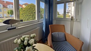 A room with a large window, a wicker chair, a radiator, and a vase of white roses. - Pension am Meer (Ostseebad Baabe)