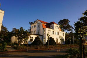 Um edifício de dois andares com telhado vermelho, rodeado por árvores e calçada.