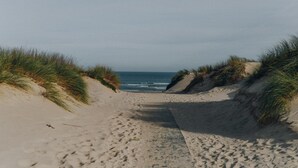 A sandy beach path leading to the ocean, flanked by grassy dunes. - Pension am Meer (Ostseebad Baabe)
