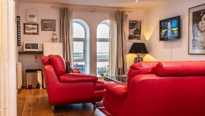 A modern living room with red leather sofas, a television, and a view of the sea through large windows. - Stunning harbour side Gold graded apartment for two with secure parking (Berwick upon Tweed)