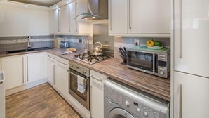 A modern kitchen with white cabinets, a stainless steel range hood, a built-in microwave, and a dishwasher. - Stunning harbour side Gold graded apartment for two with secure parking (Berwick upon Tweed)