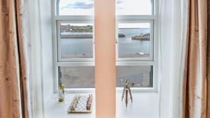 A room with a large arched window overlooking a body of water, a chessboard, and a telescope on the windowsill. - Stunning harbour side Gold graded apartment for two with secure parking (Berwick upon Tweed)