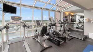Un gimnasio con máquinas de cardio, una cinta de correr y un espejo grande.