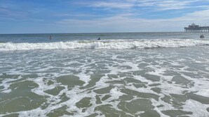 Una playa con olas, un muelle y cielo despejado.