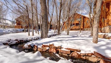 Une cabane en bois, posée sur des fondations en pierre, entourée d’un paysage enneigé et d’arbres sans feuilles.