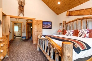 A bedroom with a wooden headboard, a bed with patterned bedding, a wooden dresser, and a door leading to another room.