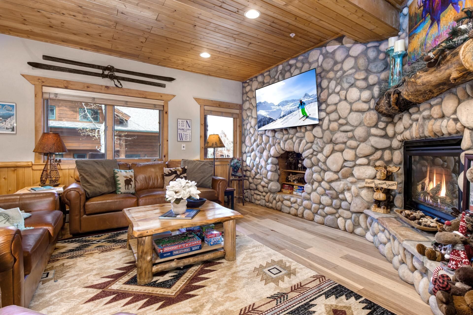 Un salon chaleureux avec une cheminée en pierre, un téléviseur fixé au mur et un plafond en bois.