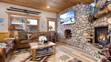 Un salon chaleureux avec une cheminée en pierre, un téléviseur fixé au mur et un plafond en bois.