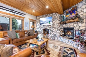 A cozy living room with a stone fireplace, a television mounted on the wall, and a leather sofa.