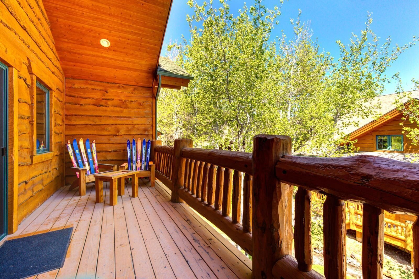 Una cabaña de madera con terraza, un banco y esquíes apoyados en la pared.