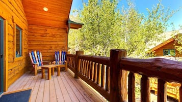 Una cabaña de madera con terraza, un banco y esquíes apoyados en la pared.