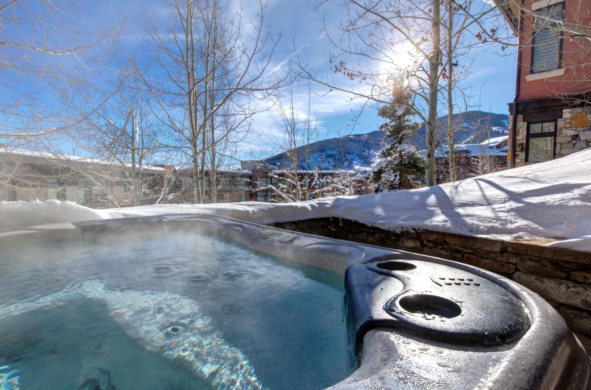 A hot tub with a stone wall, snow-covered ground, and a mountain in the background.