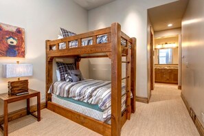 A bunk bed with a wooden frame, a bedside table with a lamp, and a bear painting on the wall.