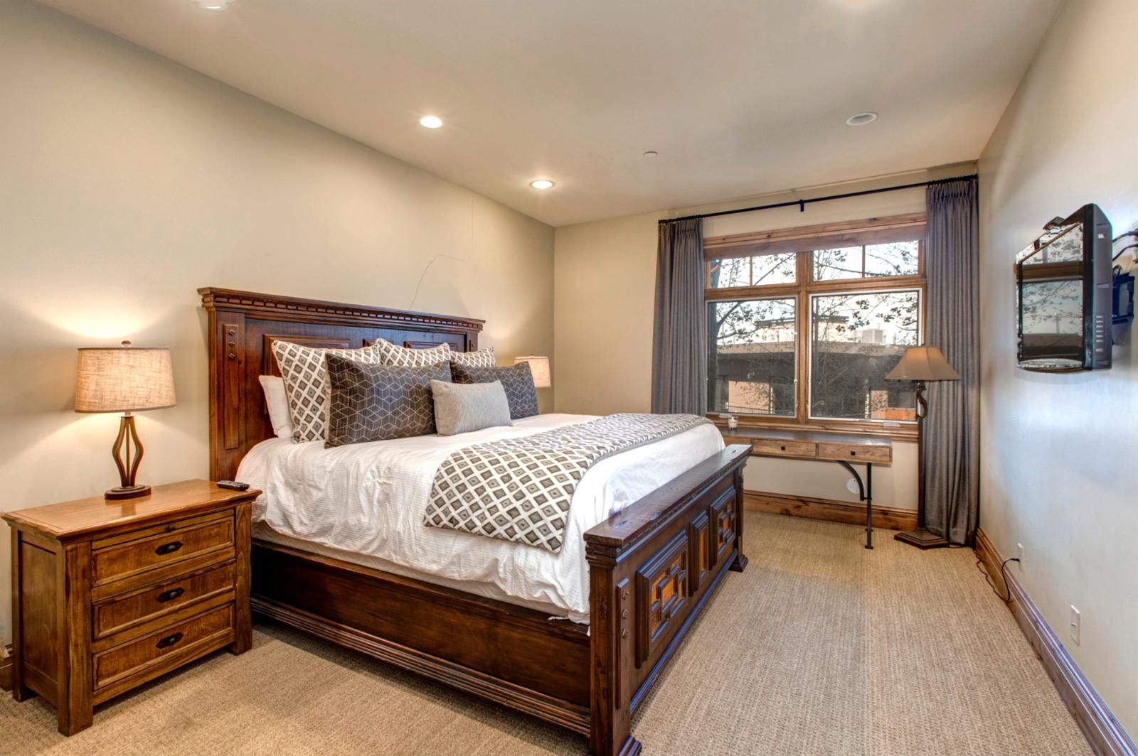 A bedroom with a wooden bed, bedside tables, a desk, and a window with curtains.