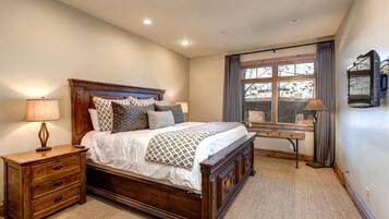 A bedroom with a wooden bed, bedside tables, a desk, and a window with curtains.