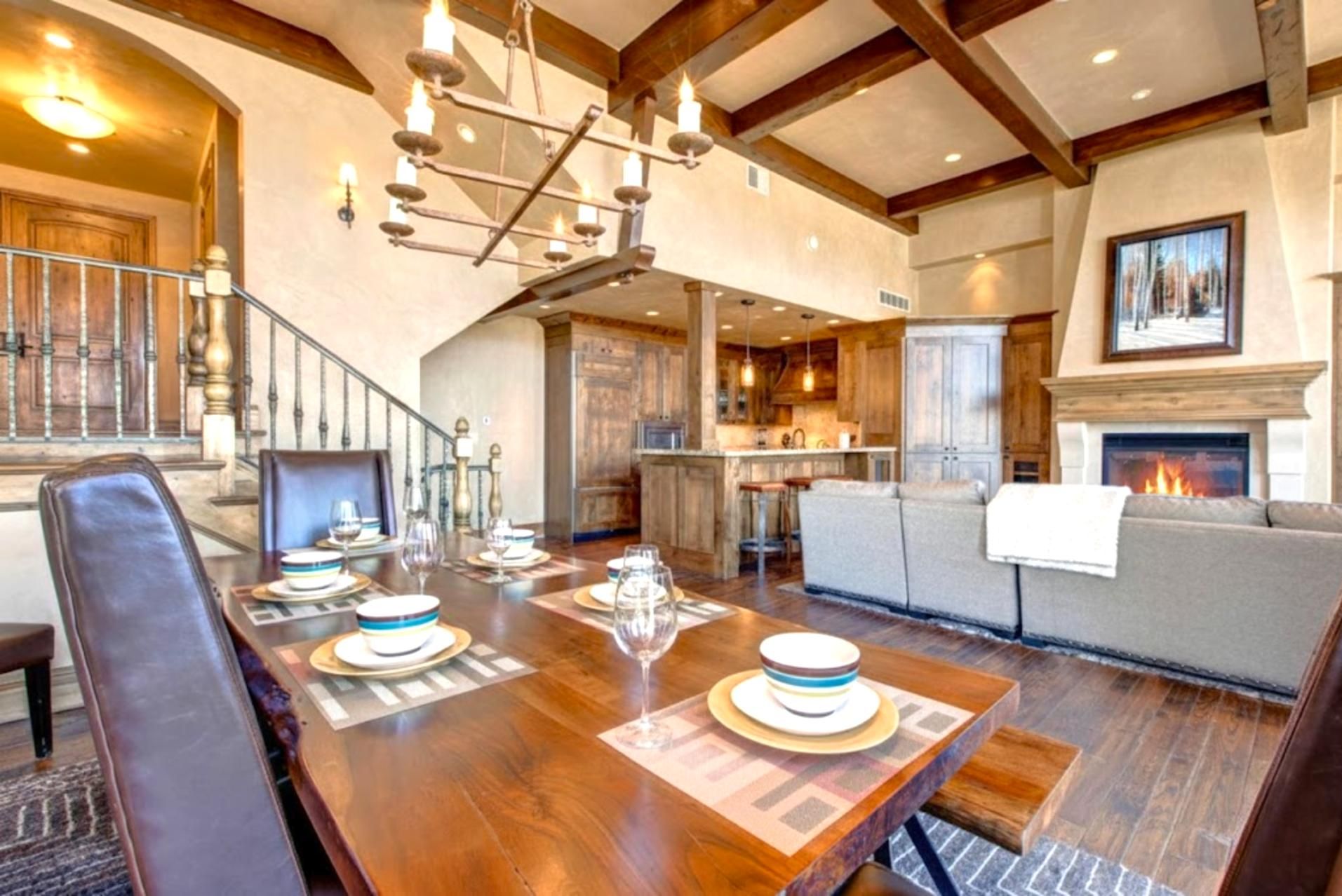 A dining area with a wooden table set for four, a fireplace, and a staircase leading to another level.