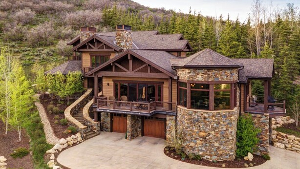 A large, multi-story log cabin with stone accents, a wrap-around deck, and a stone chimney.