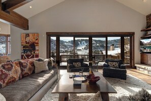 Un salon spacieux doté d’une grande fenêtre offrant une vue sur les montagnes, d’une table basse en bois et d’un canapé agrémenté de coussins à motifs.