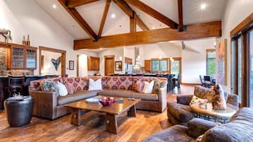 A spacious living area with a large sectional sofa, wooden flooring, and exposed wooden beams.