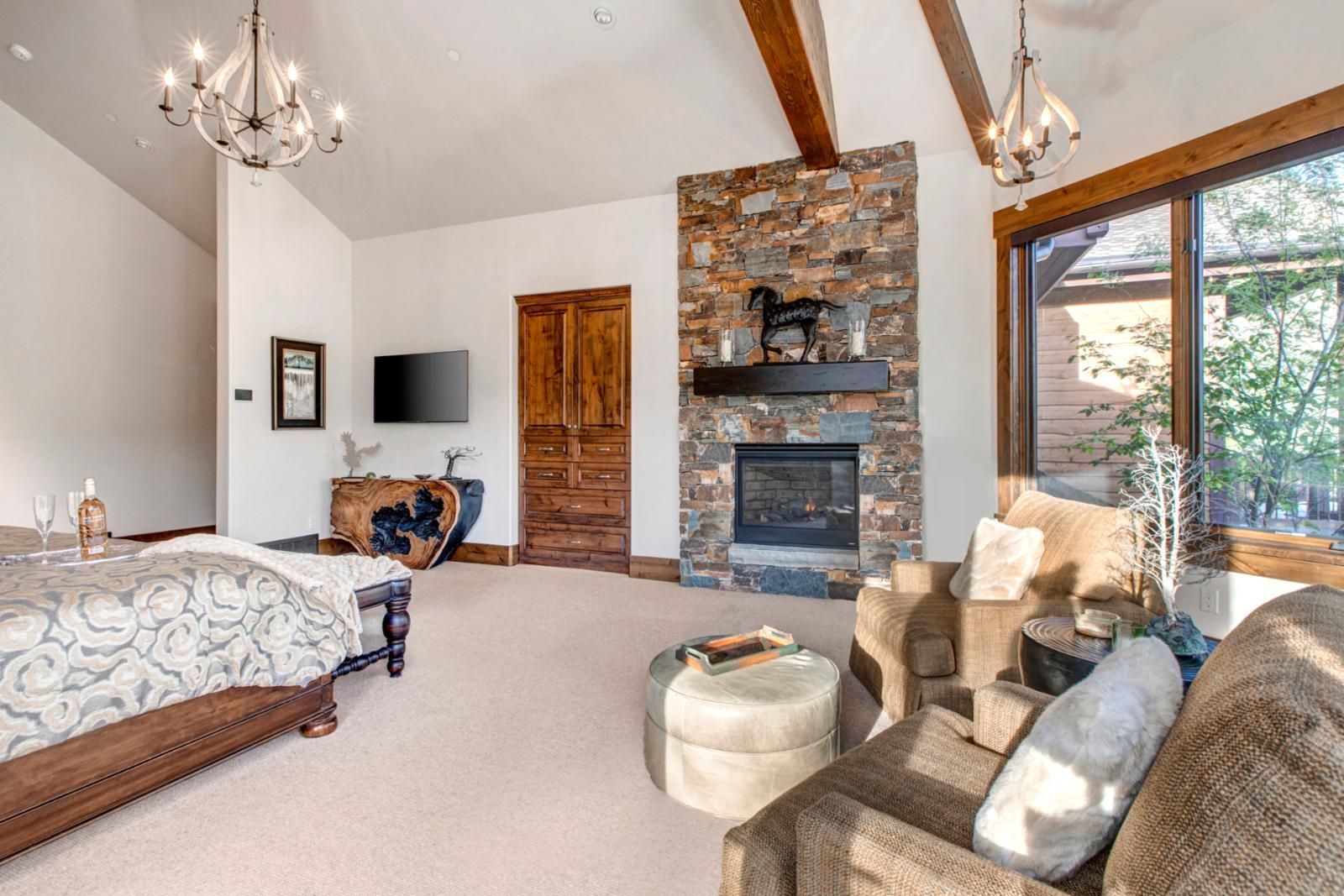 Une chambre spacieuse avec un grand lit, une cheminée en pierre et un coin salon confortable avec un canapé et un pouf.