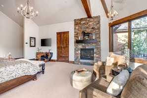 Une chambre spacieuse avec un grand lit, une cheminée en pierre et un coin salon confortable avec un canapé et un pouf.