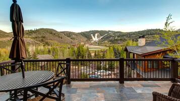 A patio with a table and chairs, a wooden fence, and a view of a valley with mountains and a building in the distance.