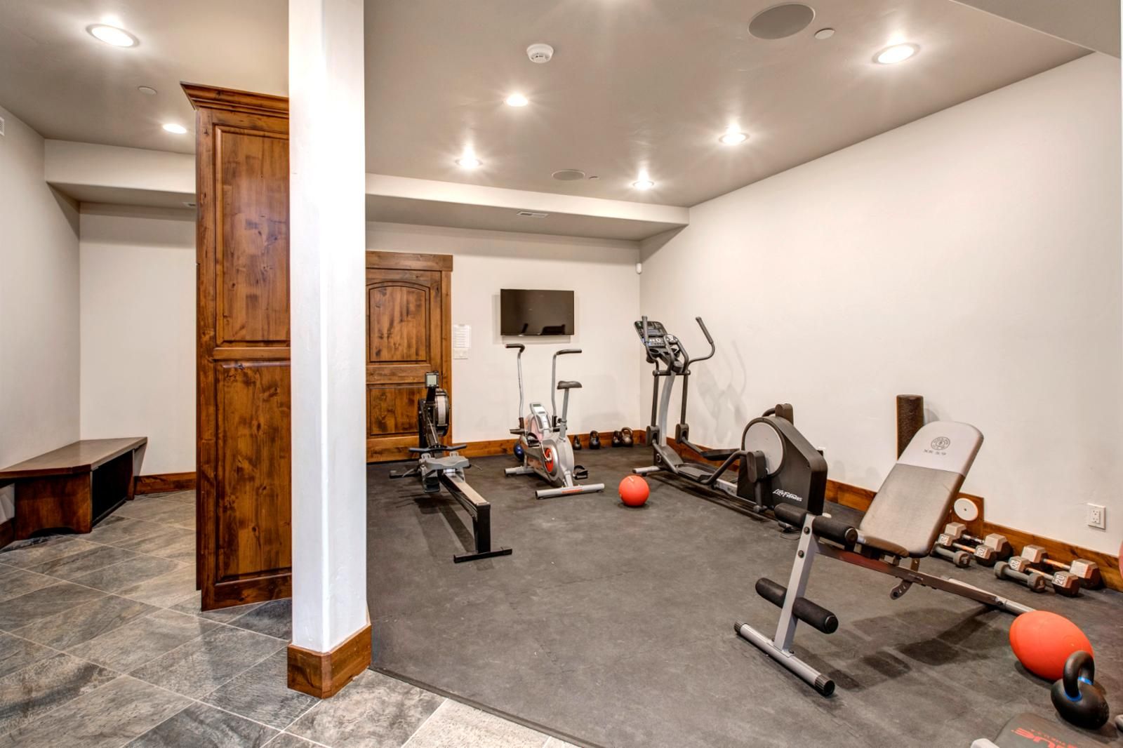 Un gimnasio con equipo de ejercicio, una banca y un televisor en la pared.