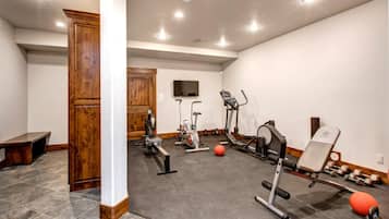 A gym with exercise equipment, a bench, and a television on the wall.