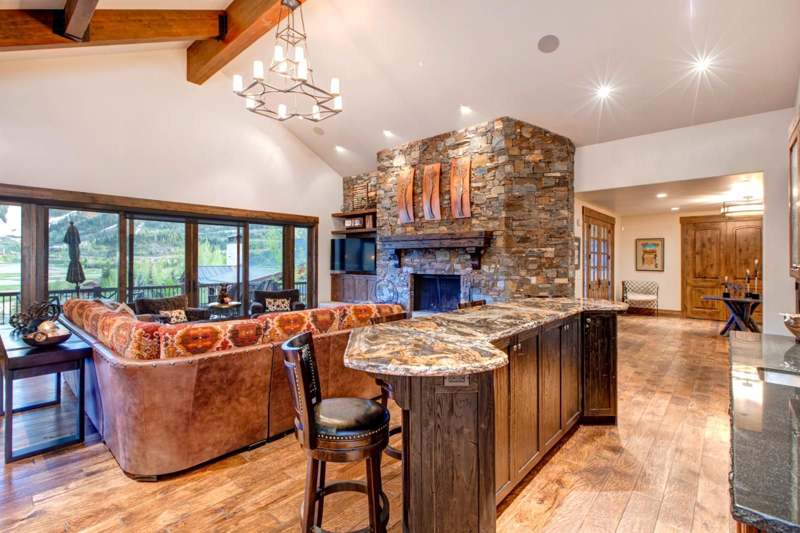 A kitchen with a stone fireplace, a bar area, and a large window overlooking a scenic landscape.