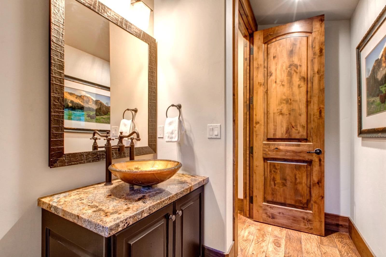 A bathroom with a wooden door, a granite countertop, and a large mirror.