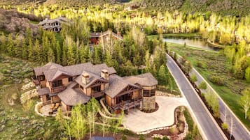 A large, multi-story lodge with a stone facade, surrounded by a forested landscape and a lake.