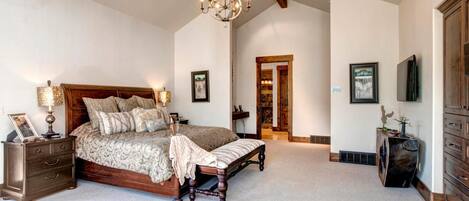 A spacious bedroom with a large bed, a chandelier, a dresser, and a television.