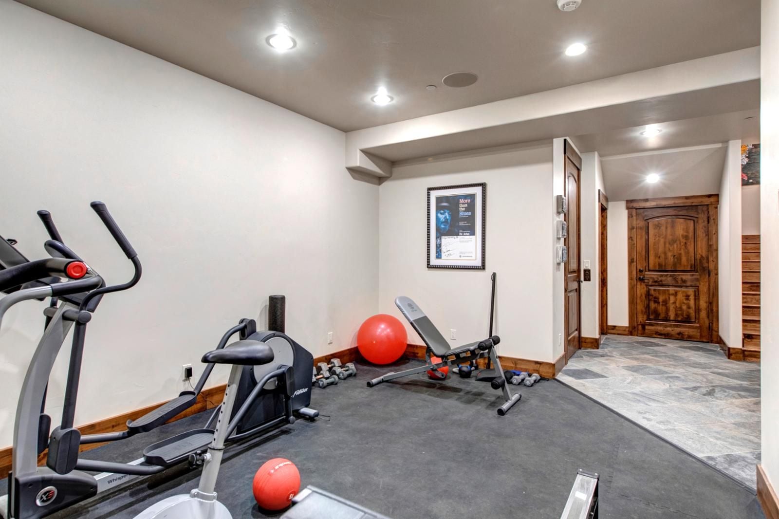 Une salle de sport à domicile équipée de matériel d’exercice, notamment des tapis de course, un banc et des poids.