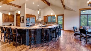A spacious kitchen with a large island, wooden bar stools, and a view through the windows.