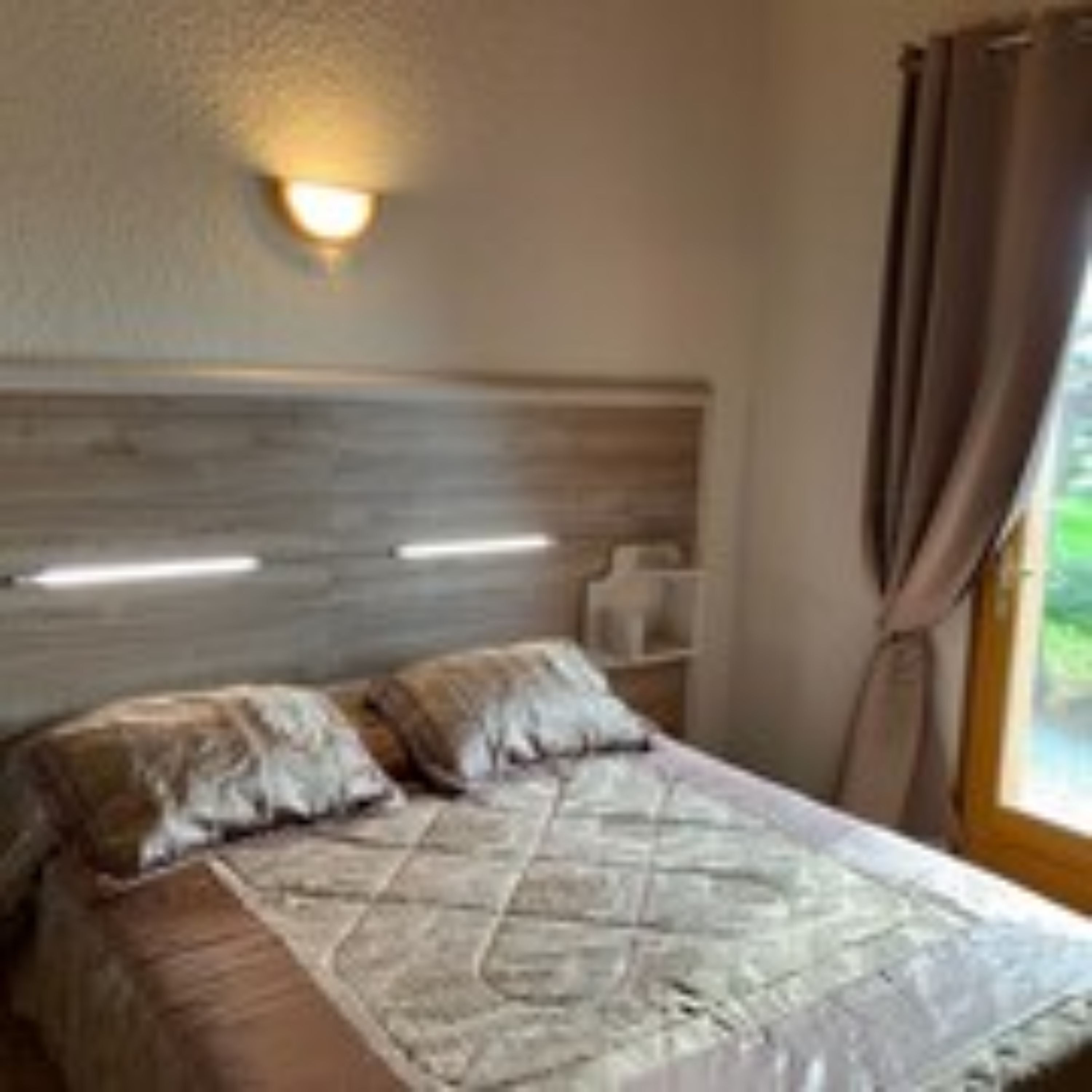 Un dormitorio con cabecera de madera, cama con cubrecama acolchado y ventana con cortinas.