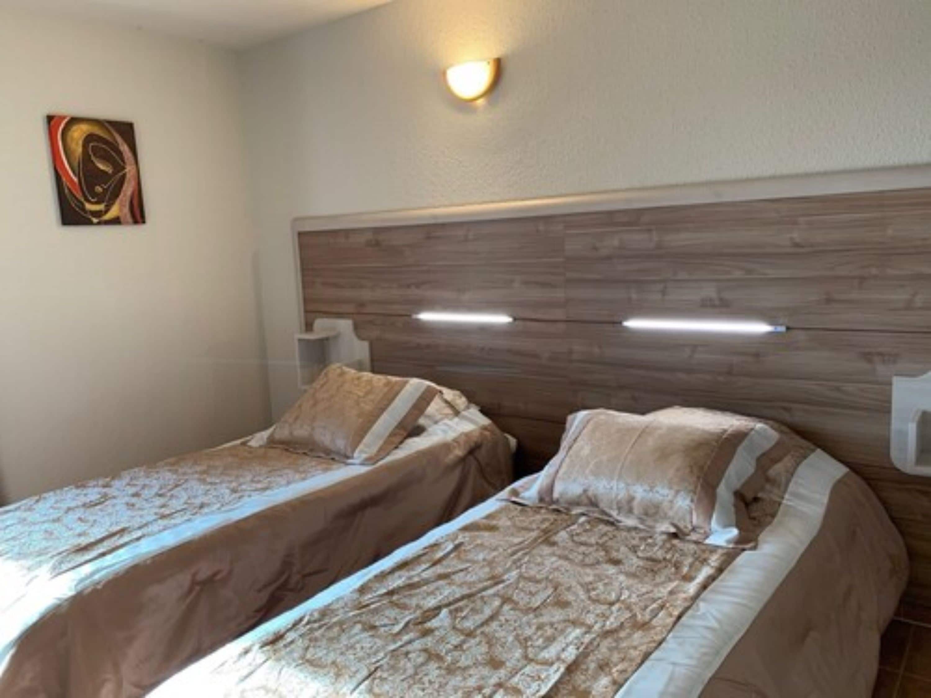 Quarto com duas camas, cabeceira de madeira, luminária na parede e um quadro.