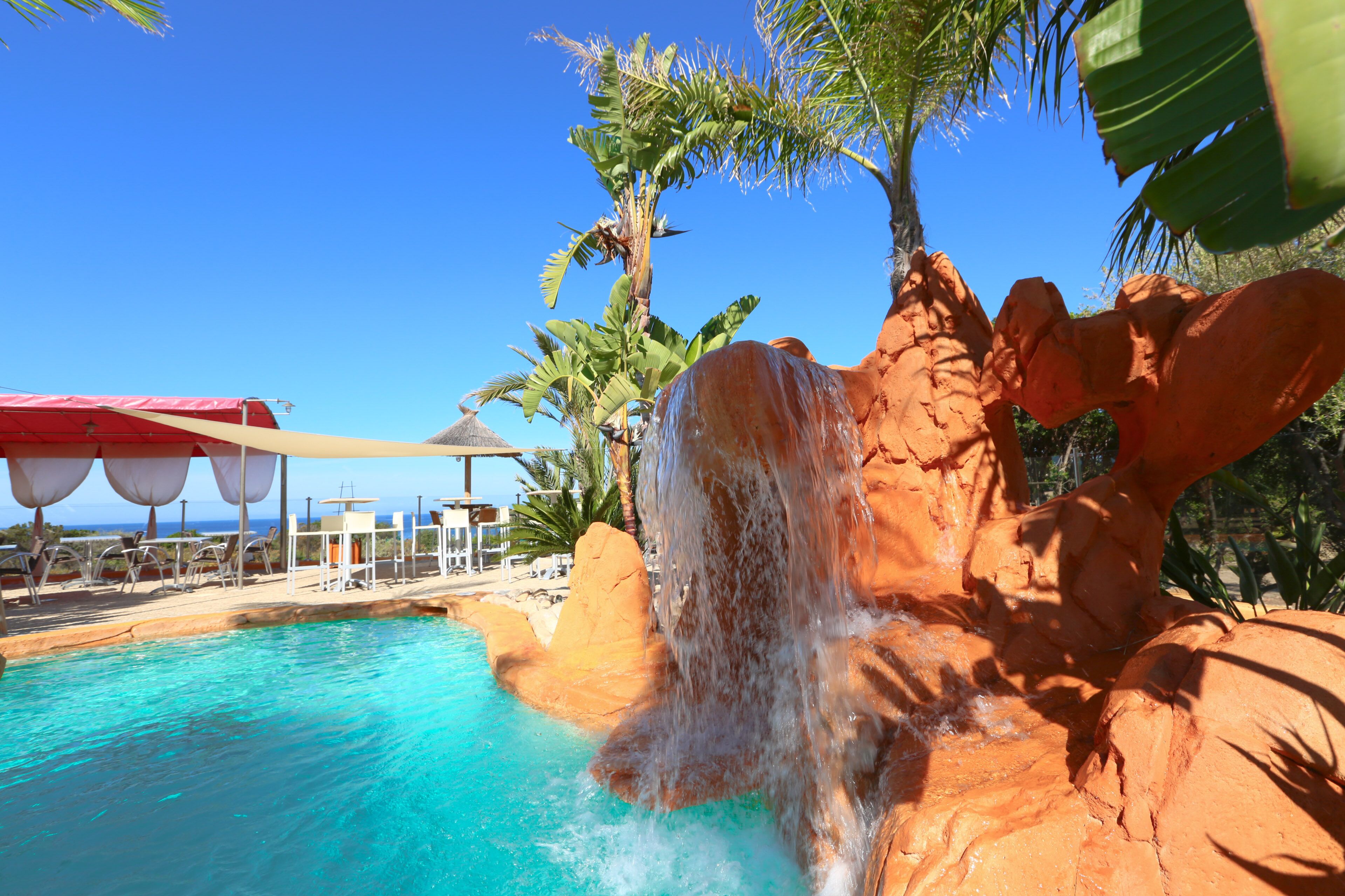 A pool with a waterfall feature, surrounded by rock formations and palm trees.