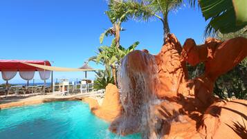 A pool with a waterfall feature, surrounded by rock formations and palm trees.
