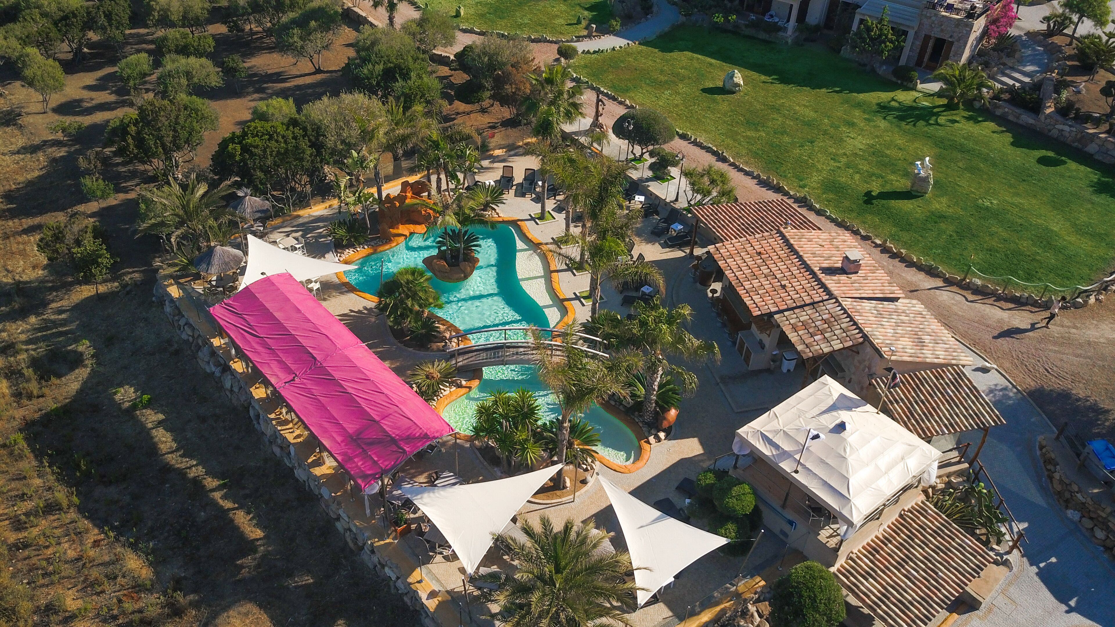An aerial view of a resort with a swimming pool, lounge areas, and a bridge connecting different sections.