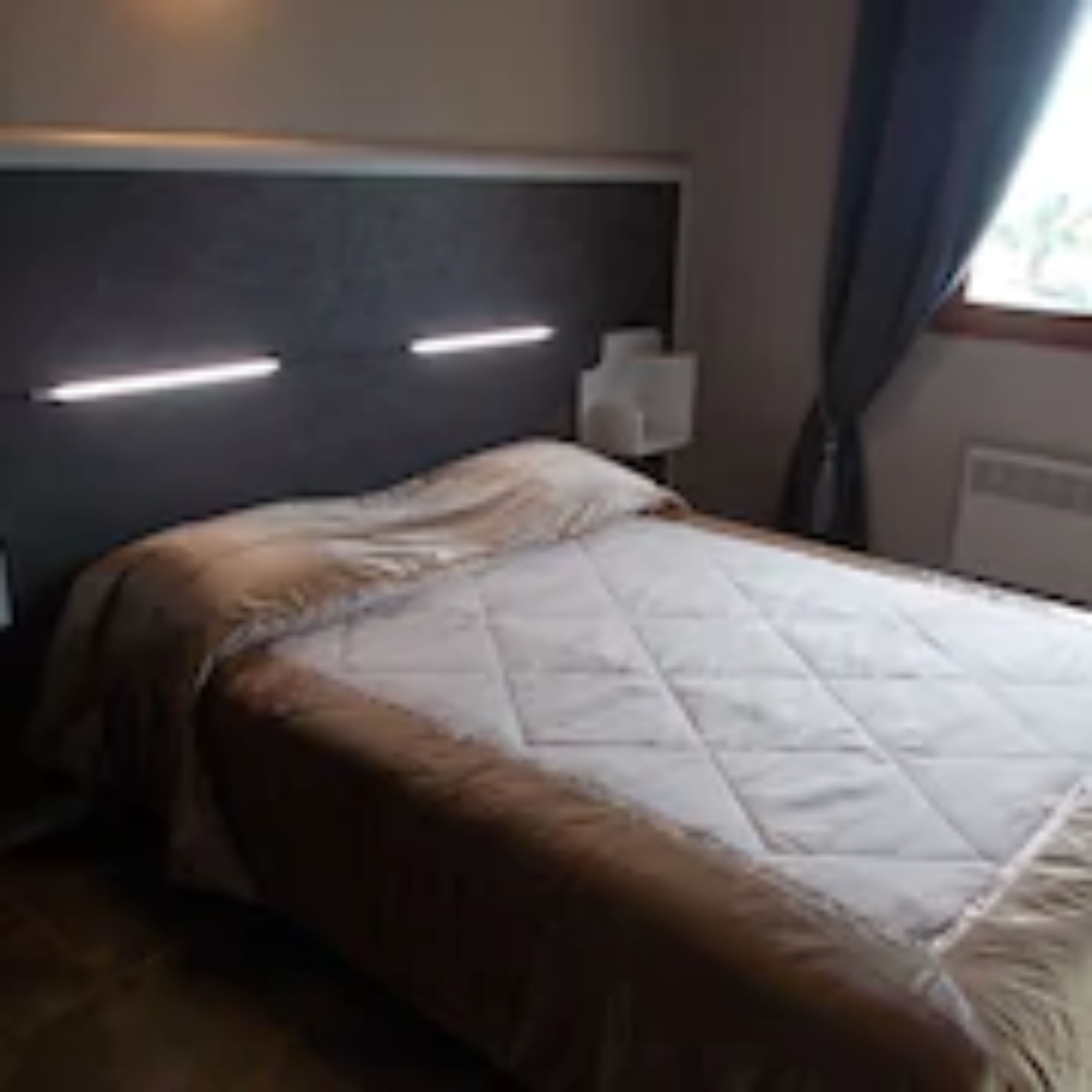 A hotel room with a bed, a bedside table, and a window with curtains.