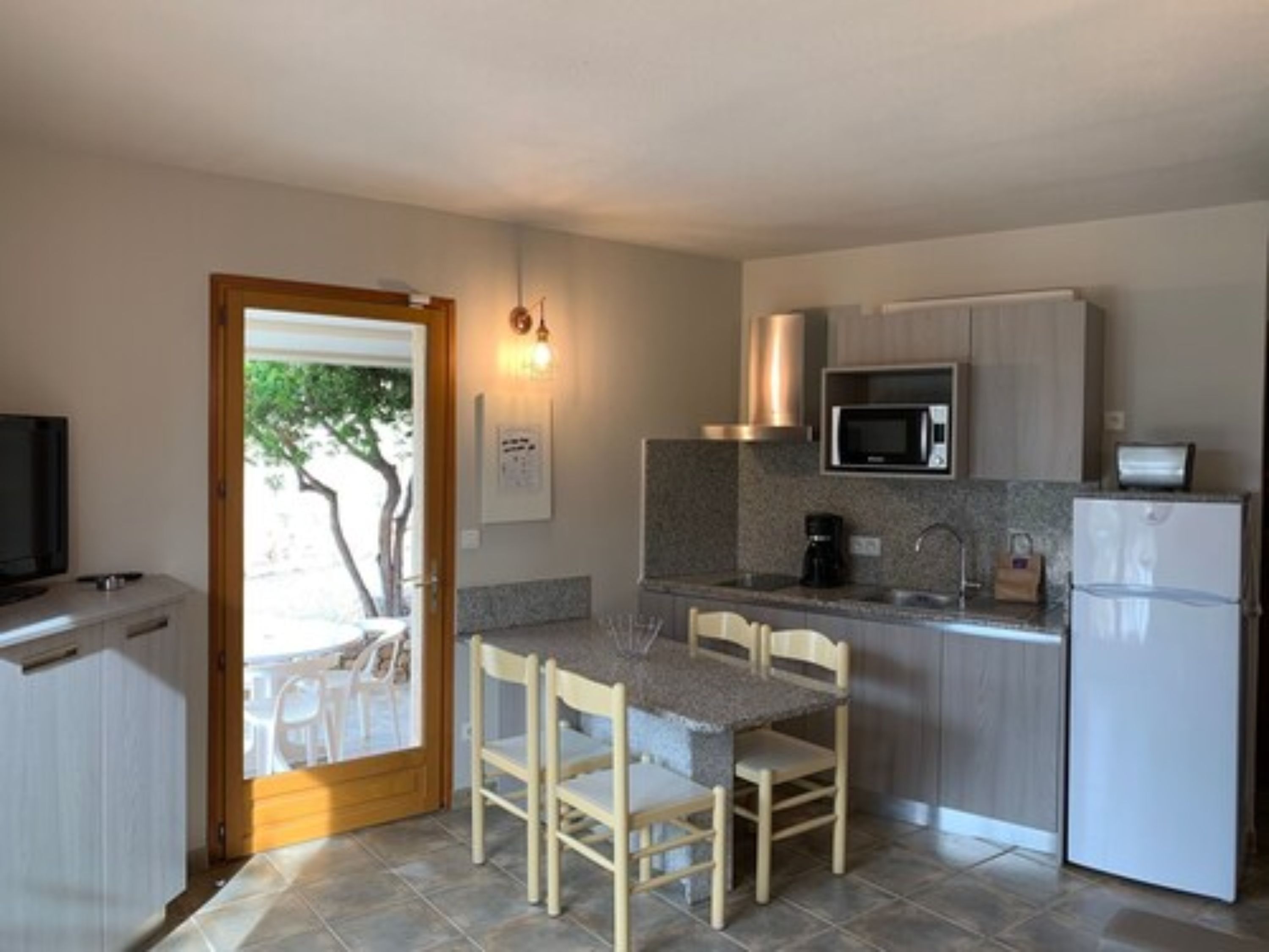 A compact kitchen with a microwave, coffee maker, and refrigerator. There is a dining table with chairs and a TV in the adjacent room.