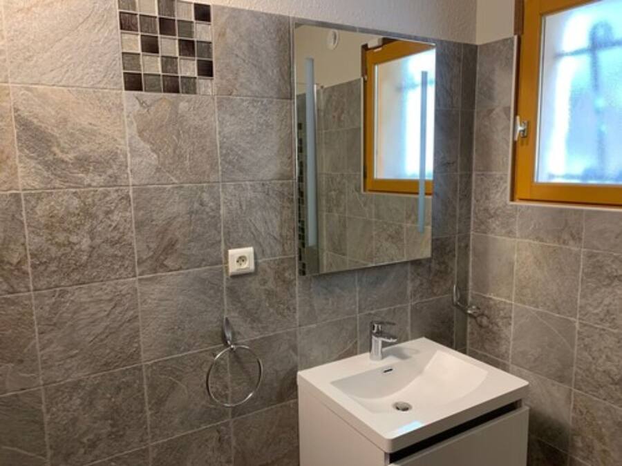 Un baño con un lavamanos blanco, un espejo y un tozaletas.