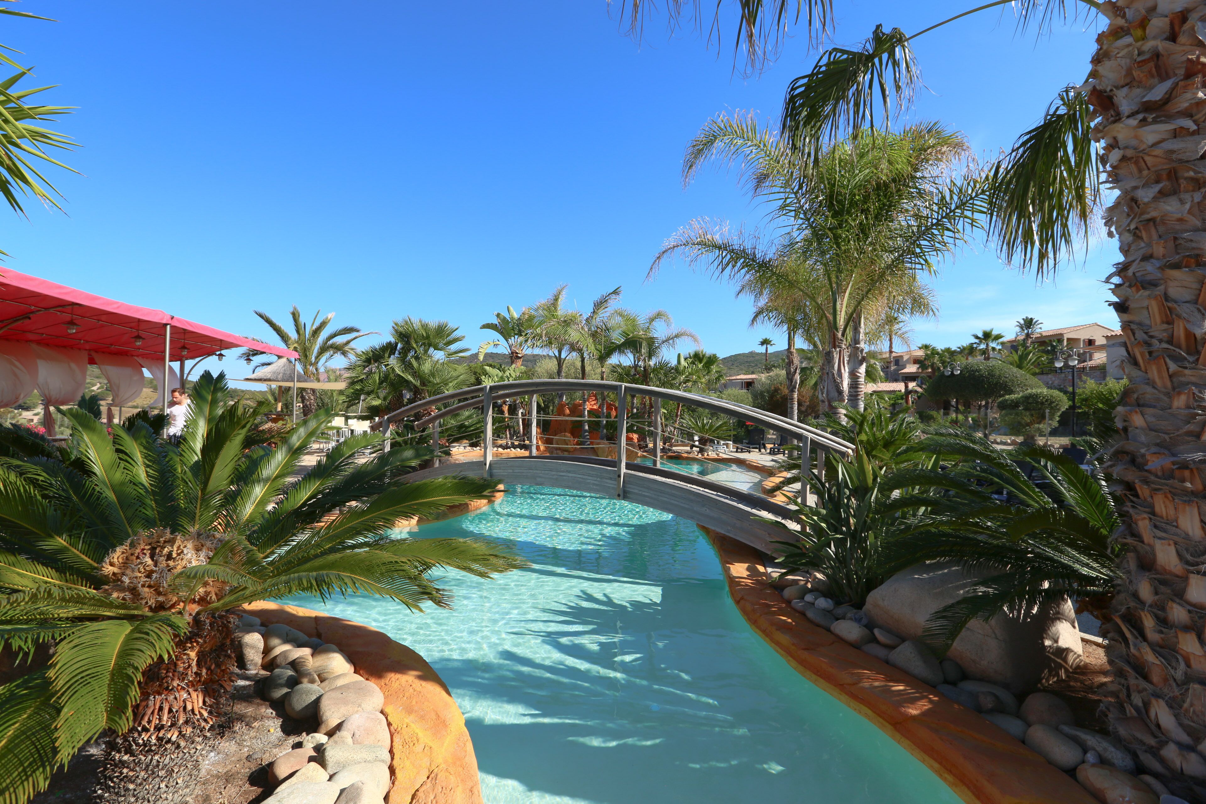 A pool area with a bridge, palm trees, and a red canopy.