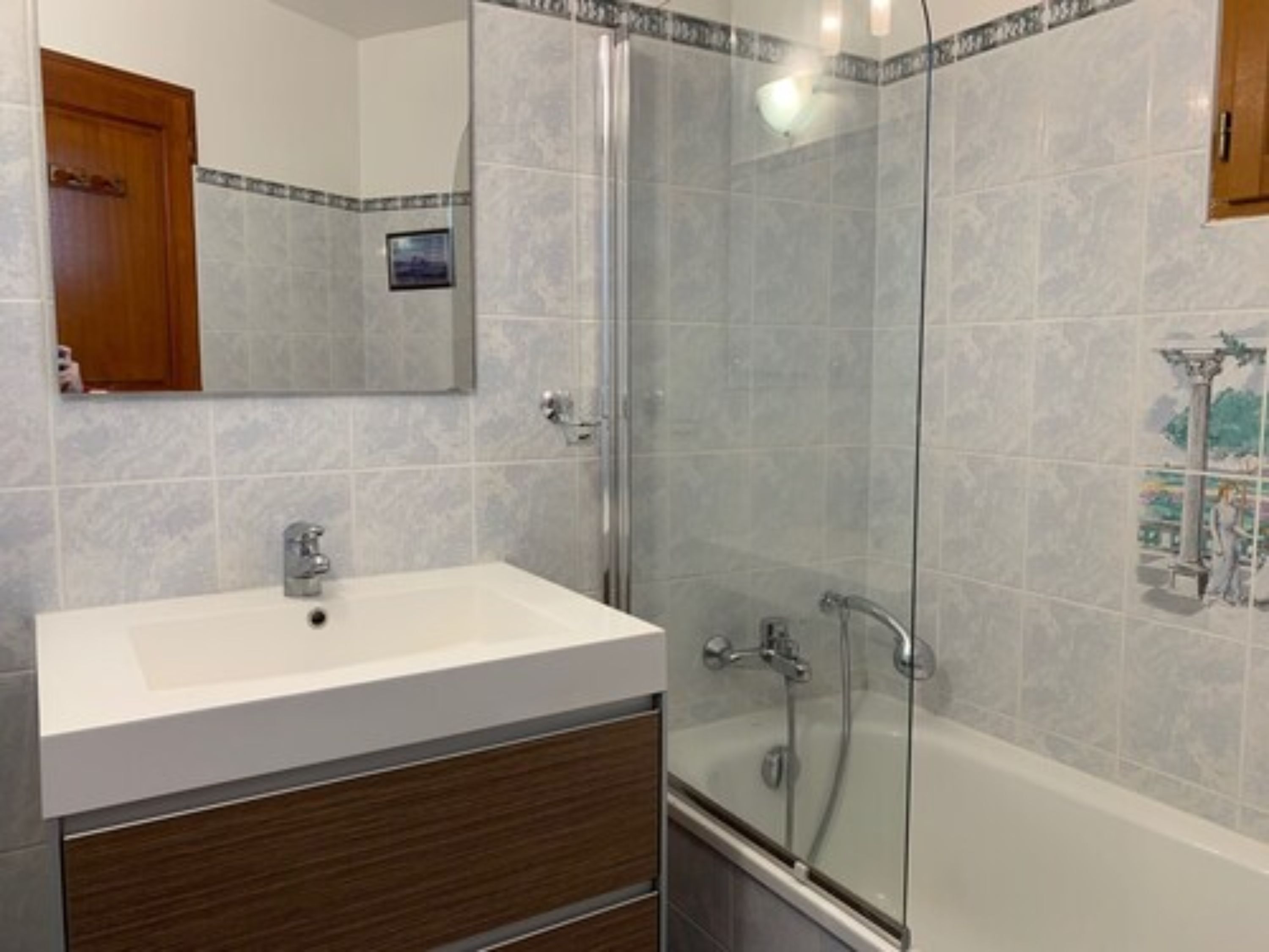 Een badkamer met een douche met glazen wanden, een witte wastafel en een houten wastafelmeubel.