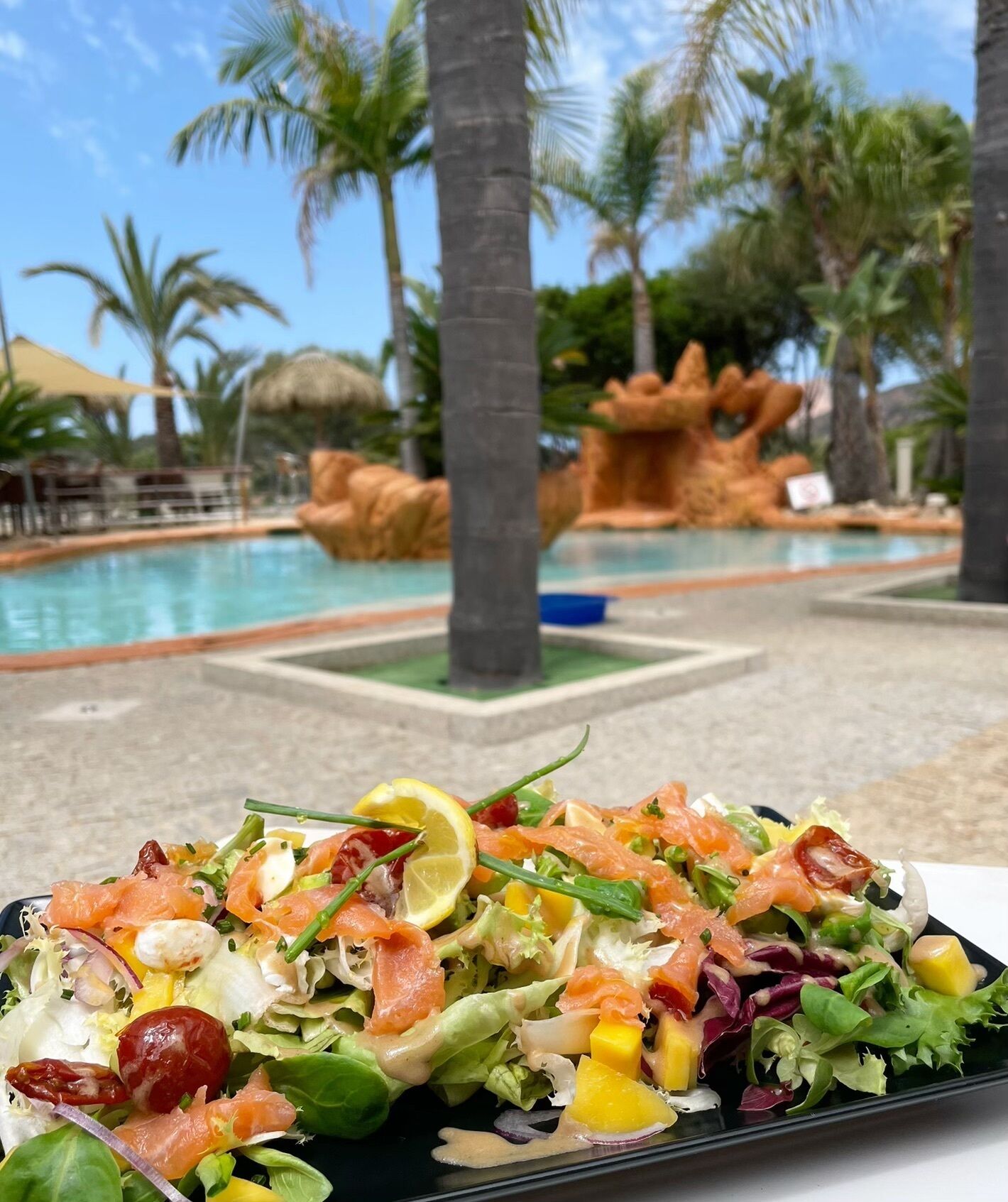 A poolside view with a dining table and a salad in the foreground.