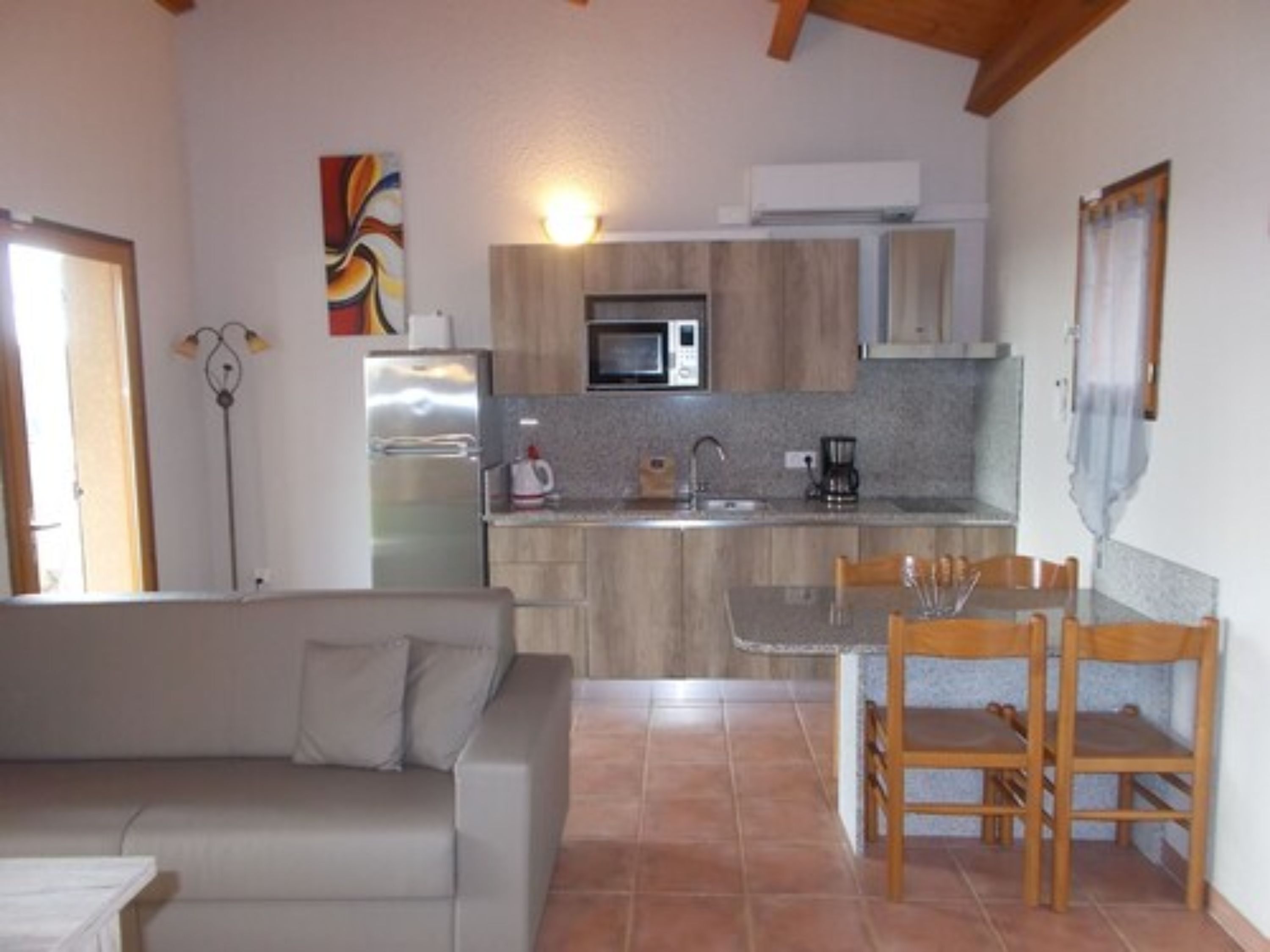 Cocina compacta con microondas, refrigerador y cafetera. Cuenta con un comedor con mesa y sillas.
