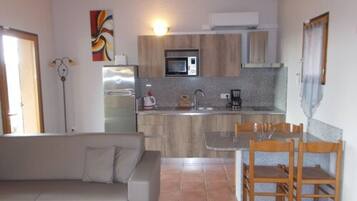 Cocina compacta con microondas, refrigerador y cafetera. Cuenta con un comedor con mesa y sillas.