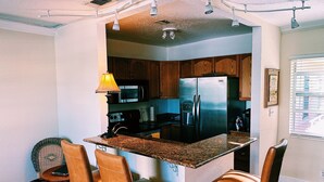 A kitchen with a central island, bar stools, a microwave, and a refrigerator.