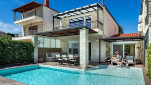 Une maison moderne à deux étages dotée d’une piscine, d’un espace salon extérieur et d’un patio couvert.