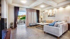 Un salon moderne avec un canapé, une table basse et un téléviseur. On aperçoit un coin repas avec une table et des chaises à travers une porte vitrée.